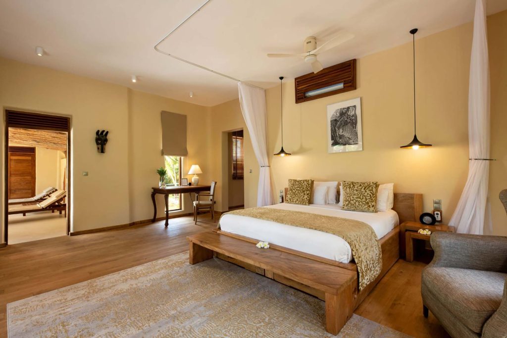 Modernes Hotelzimmer mit Doppelbett, Holzmöbeln, Teppich und Balkon mit Holzliegen in Sansibar