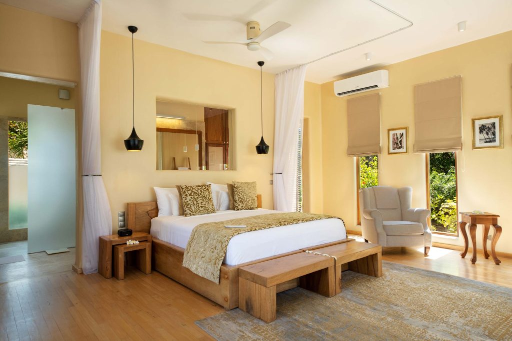 Geräumiges Hotelzimmer mit großem Bett, hellem Holz, cremefarbenen Wänden und drei großen Fenstern