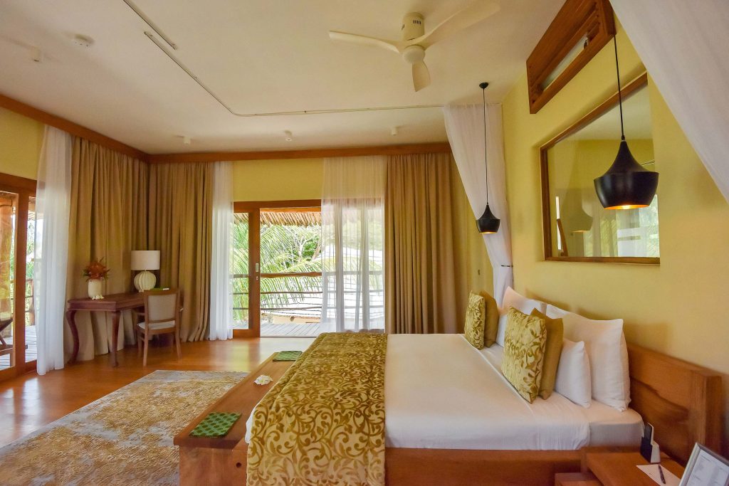 Geräumiges Hotelzimmer mit Doppelbett, hellem Holzmöbeln, Holzboden und Balkon mit Grünblick in Sansibar