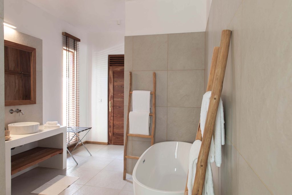 Modernes Badezimmer mit freistehender Badewanne, Holzleiter, Waschtisch und Fenster mit Holzjalousien in Sansibar