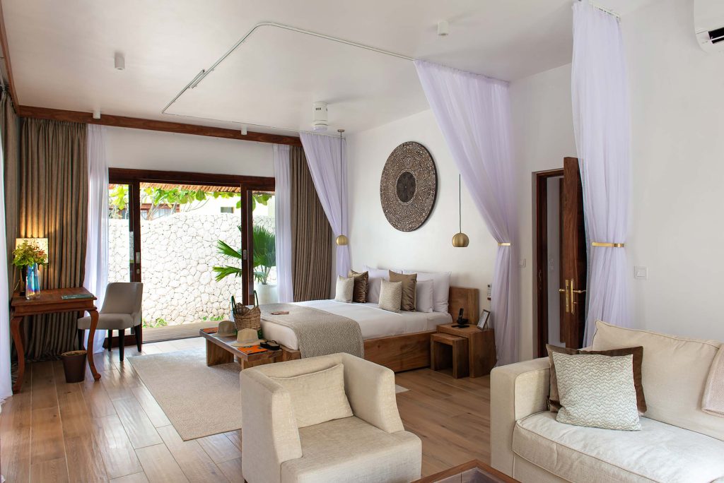 Hotelzimmer in Zanzibar White Sand Luxury Villas mit großem Bett, Sofa, hellem Holz und weiß-beigen Farbtönen