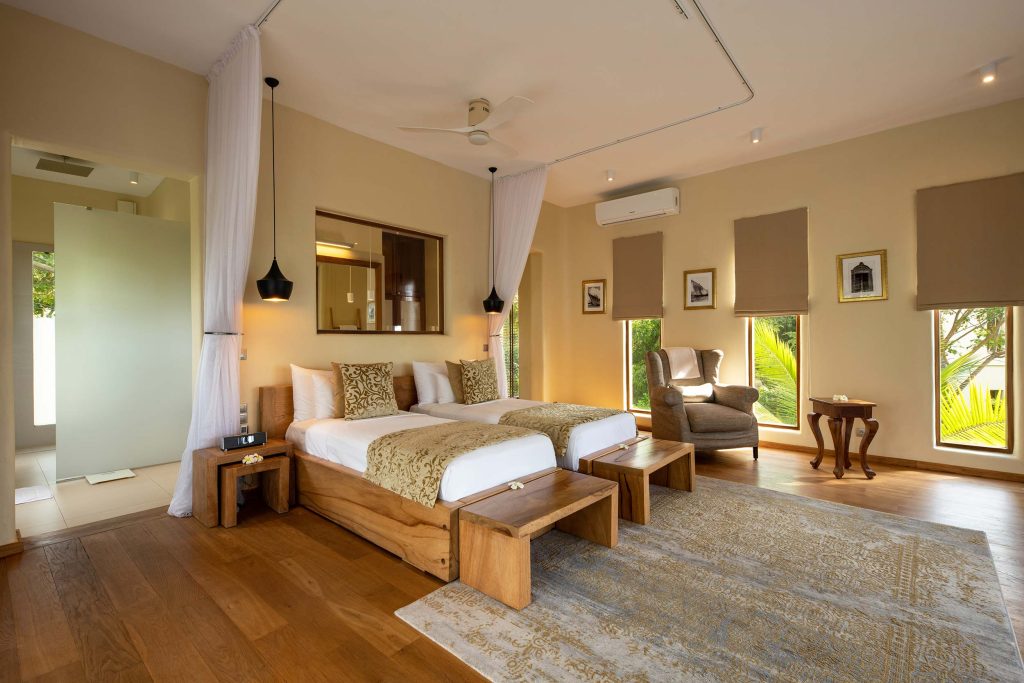 Hotelzimmer mit zwei parallel stehenden Holzbetten, bodentiefen Fenstern und offener Glaswand