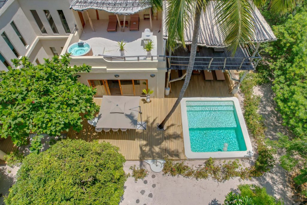Vogelperspektive auf Terrasse mit rechteckigem Pool, Whirlpool, Sonnenschirm und Holzterrasse umgeben von grünem Laub