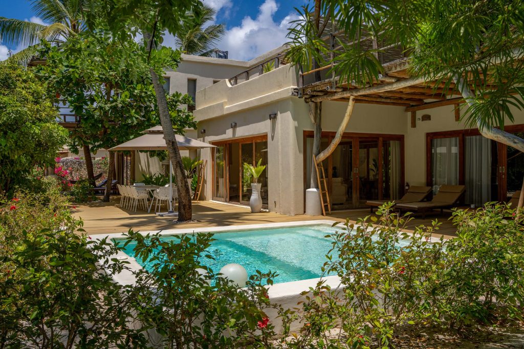 Außenbereich des Zanzibar White Sand Luxury Villas & Spa mit Pool, Esstisch, Stühlen und tropischer Vegetation