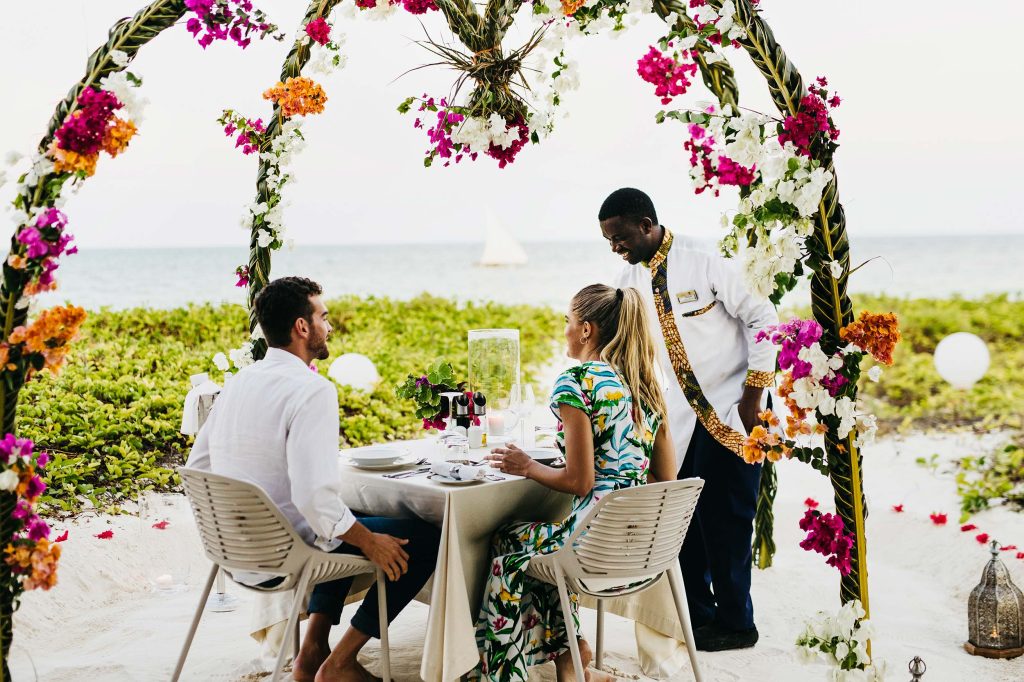 Paar bei romantischem Outdoor-Dinner am Strand mit geschmücktem Torbogen