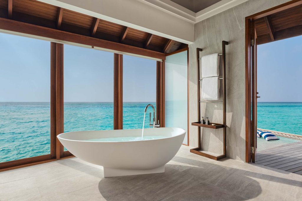 Badezimmer mit freistehender Badewanne und großen Glasfenstern mit Blick auf das türkisfarbene Meer