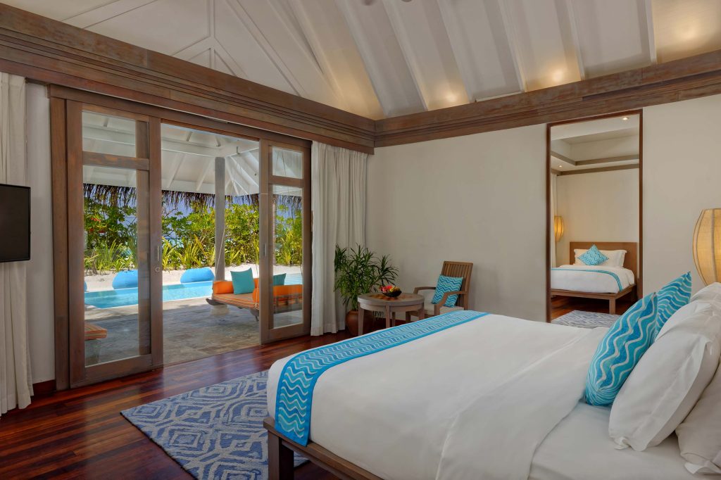 Hotelzimmer mit großem Bett, weißer und türkisfarbener Bettwäsche, Glaswand zur Terrasse mit Pool und tropischen Pflanzen
