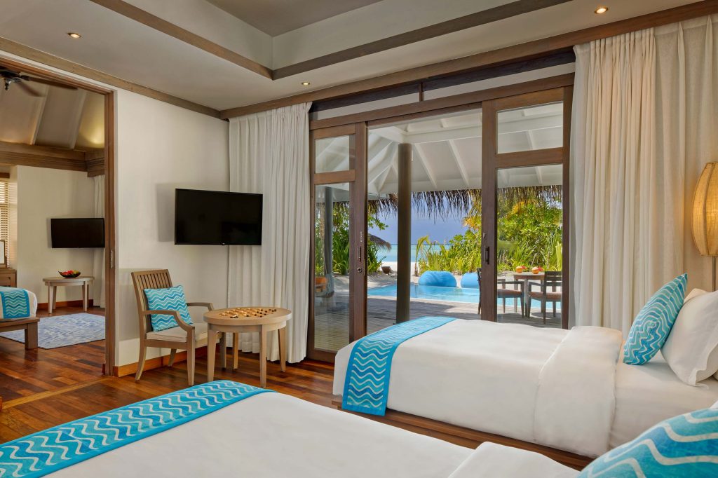 Modernes Hotelzimmer mit zwei Einzelbetten, Holzfußboden, Glasschiebetüren zur Terrasse mit Pool und tropischer Vegetation