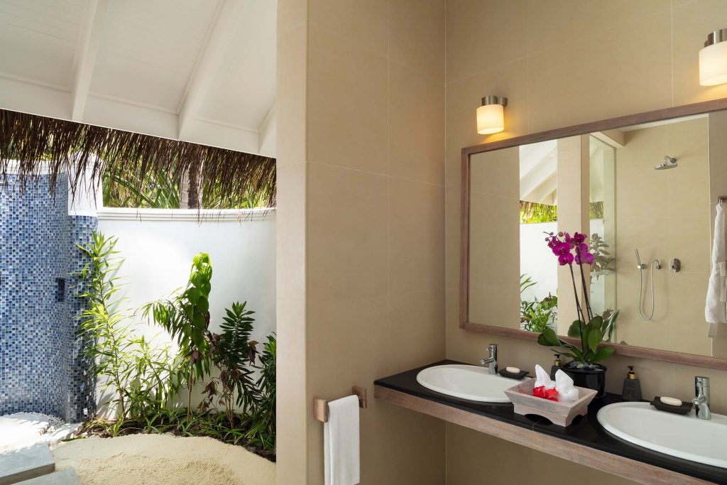 Badezimmer mit weißem Doppelwaschbecken auf schwarzer Arbeitsplatte, Holzgestell, blauen Mosaikfliesen und offenem.