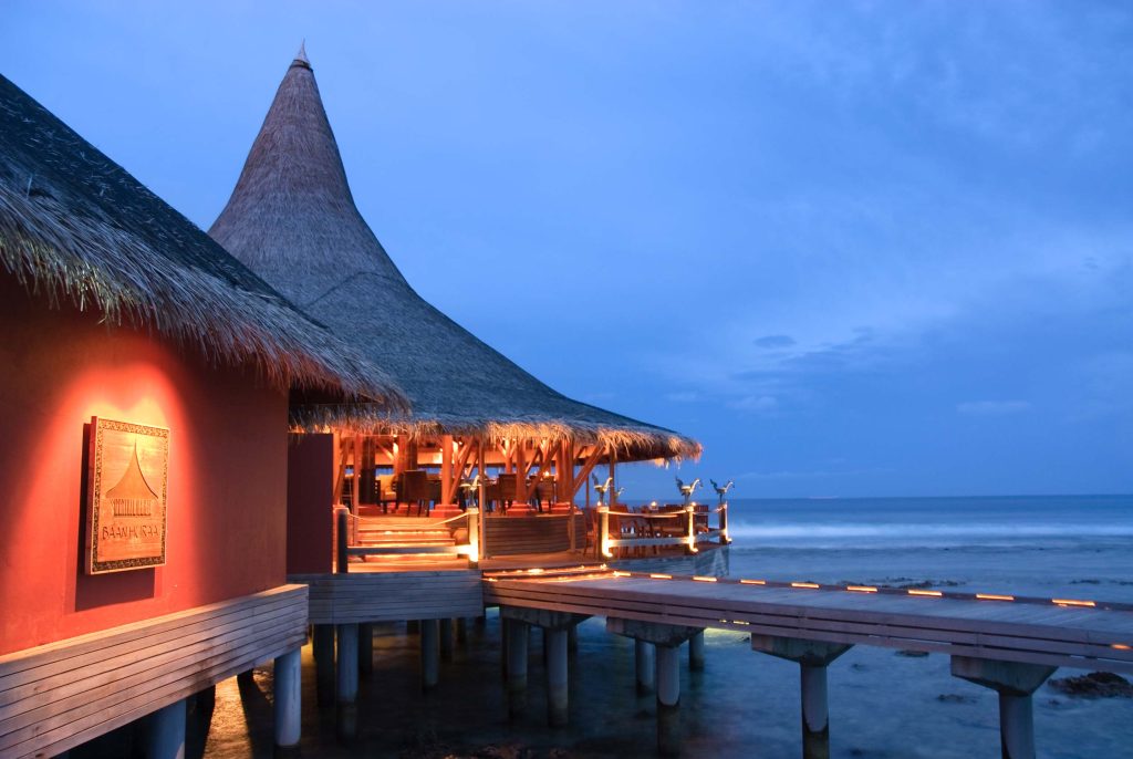 Restaurantgebäude aus Holz und Palmblättern auf Stelzen über dem Meer bei Dämmerung auf den