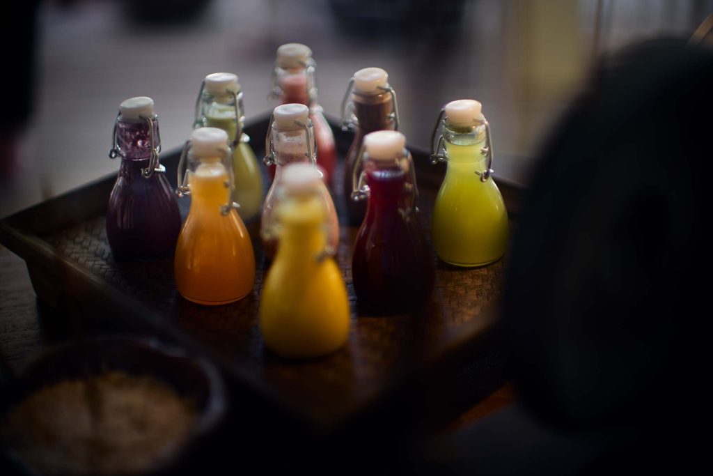 Mehrere kleine Glasflaschen mit Bügelverschluss und farbigen Flüssigkeiten auf geflochtenem Tablett
