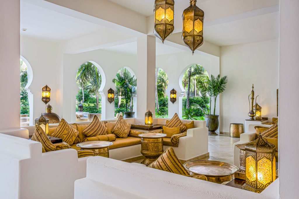 Helle Hotel-Lounge mit großen Bögen, Sofas mit gelben Kissen und Metalltischen im Baraza Resort & Spa
