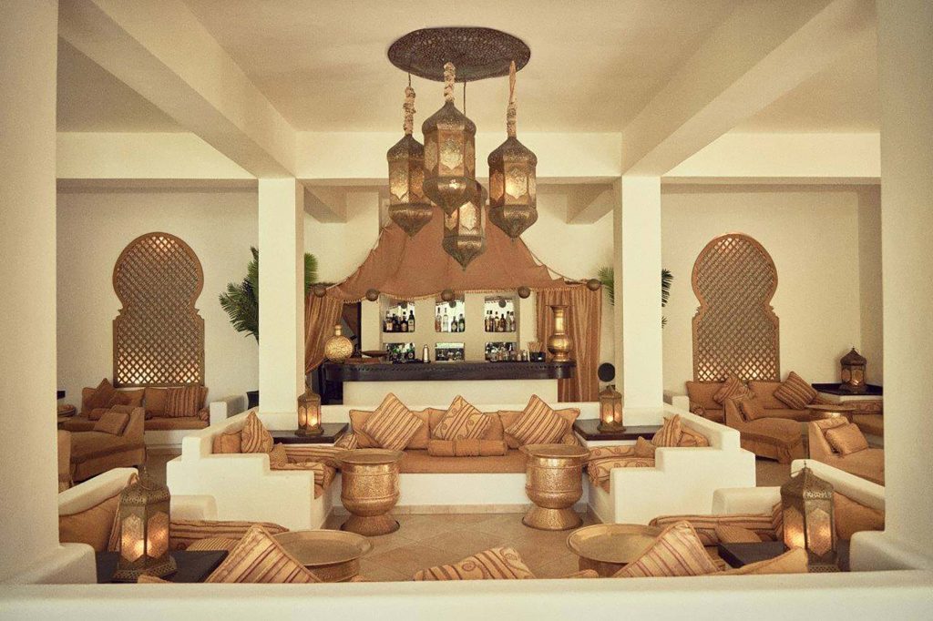 Hotel-Lounge mit weißen Sofas, braunen Kissen, verzierten Metalltischen, Holzgittern und Bar in Sansibar