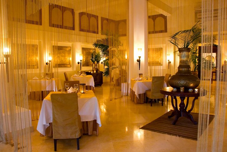 Restaurant im Baraza Resort & Spa mit runden Holztischen, weißen Tischdecken, beigen Stühlen