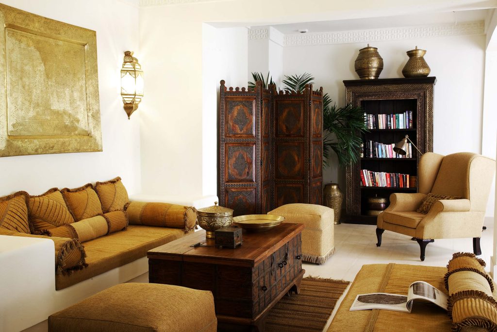 Raum mit cremefarbenem Sofa, senfgelben Kissen, dunklem Holztisch und geschnitztem Raumteiler im Baraza Resort & Spa