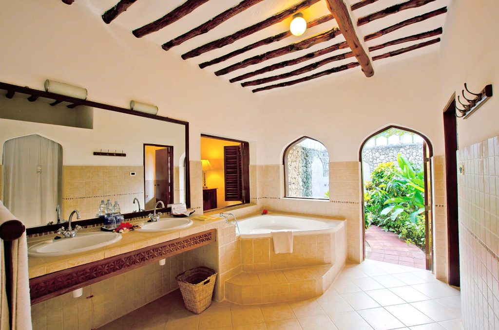 Badezimmer mit großer runder Badewanne, Doppelwaschbecken, Holzdecke und bogenförmigen Fenstern im Bluebay Beach Resort.