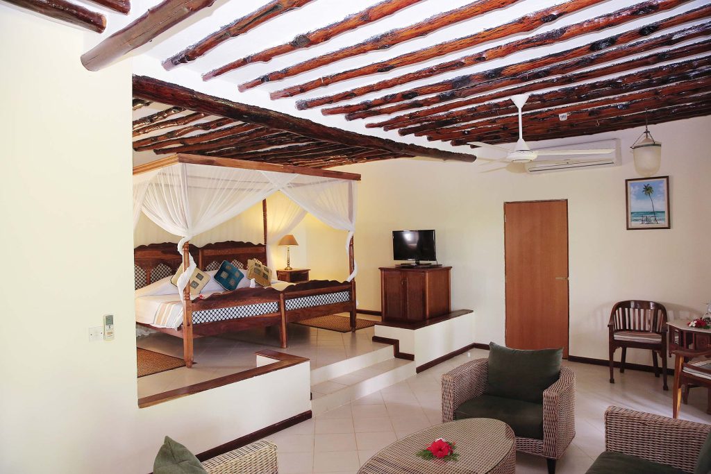 Hotelzimmer mit erhöhtem Schlafbereich, Himmelbett mit weißen Vorhängen, dunkle Holzdecke und Flachbildfernseher