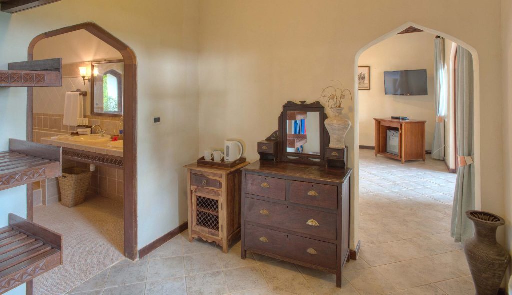 Innenraum mit hölzerner Kommode, offener Badezimmertür mit Erdtönen und Tageslicht in Bluebay Beach Resort Sansibar