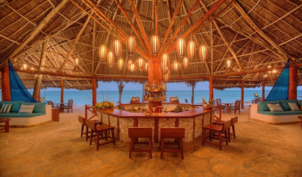 Offene Strandbar mit rundem Holz-Stein-Tresen, Barhockern und Blick auf das Meer bei Dämmerung