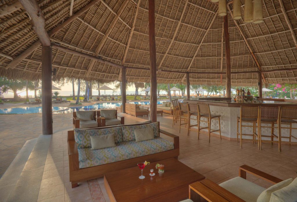 Offener Barbereich mit Strohdach, Holzsäulen und Blick auf Pool und Gartenanlage im Bluebay Beach Resort & Spa
