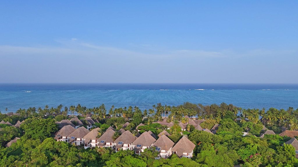 Sammlung von Bungalows mit Strohdächern und Palmen an der Küste des Bluebay Beach Resort & Spa auf Sansibar