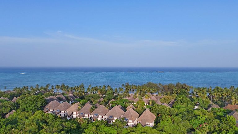 Sammlung von Bungalows mit Strohdächern und Palmen an der Küste des Bluebay Beach Resort & Spa auf Sansibar