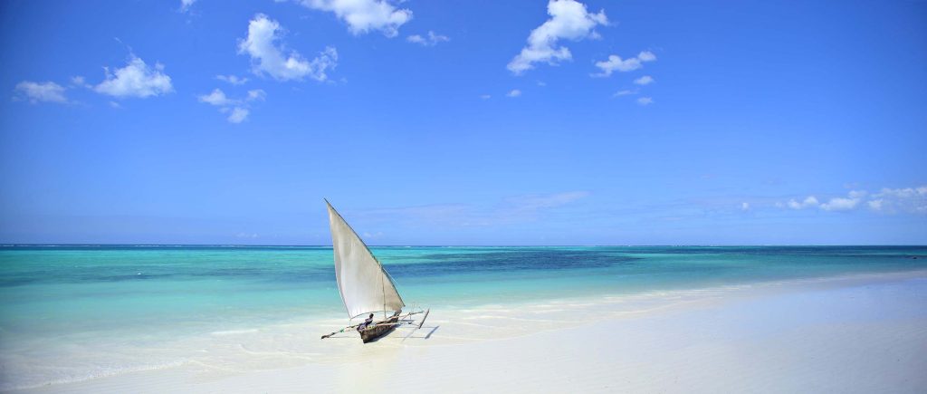 Weißer Sandstrand am Bluebay Beach Resort & Spa mit traditionellem Segelboot und türkisblauem Meer in Sansibar