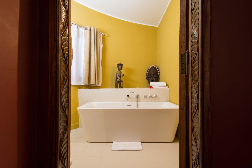 Badezimmer mit weißer freistehender Badewanne, gelben Wänden und geschnitzter Holztürrahmung