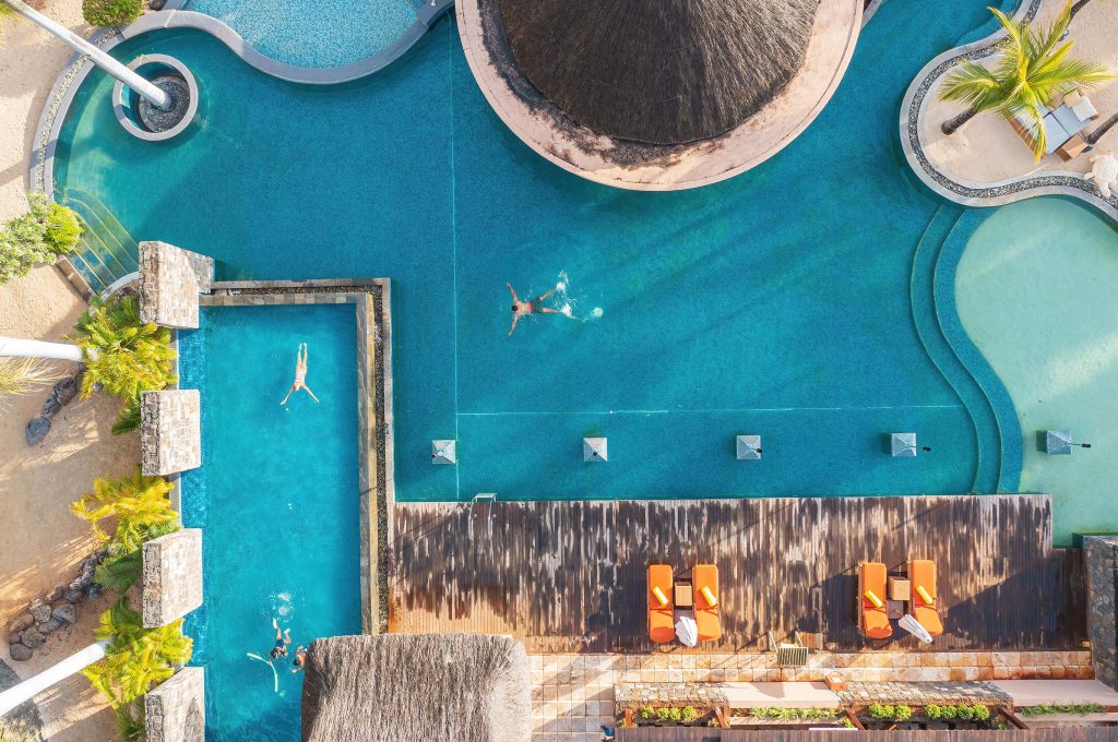 Vogelperspektive auf Poolbereich mit großem türkisfarbenem Pool, separatem rechteckigem Pool und Liegestühlen auf Holzdeck