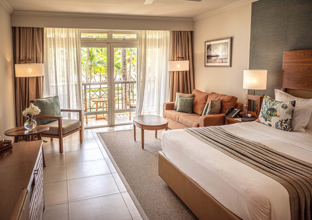 Hotelzimmer mit großem Bett, Holzmöbeln, Couch, Sessel und Balkon mit Palmen auf Mauritius