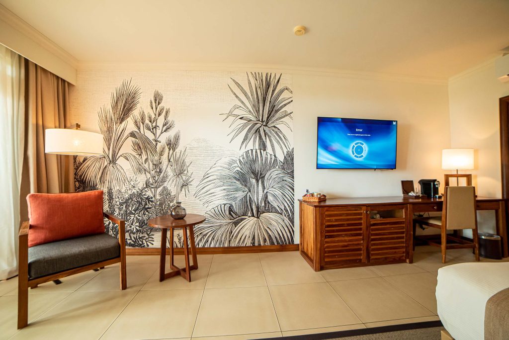Hotelzimmer mit Holzanrichte, Flachbildfernseher, Sessel mit rotem Kissen und Holztisch