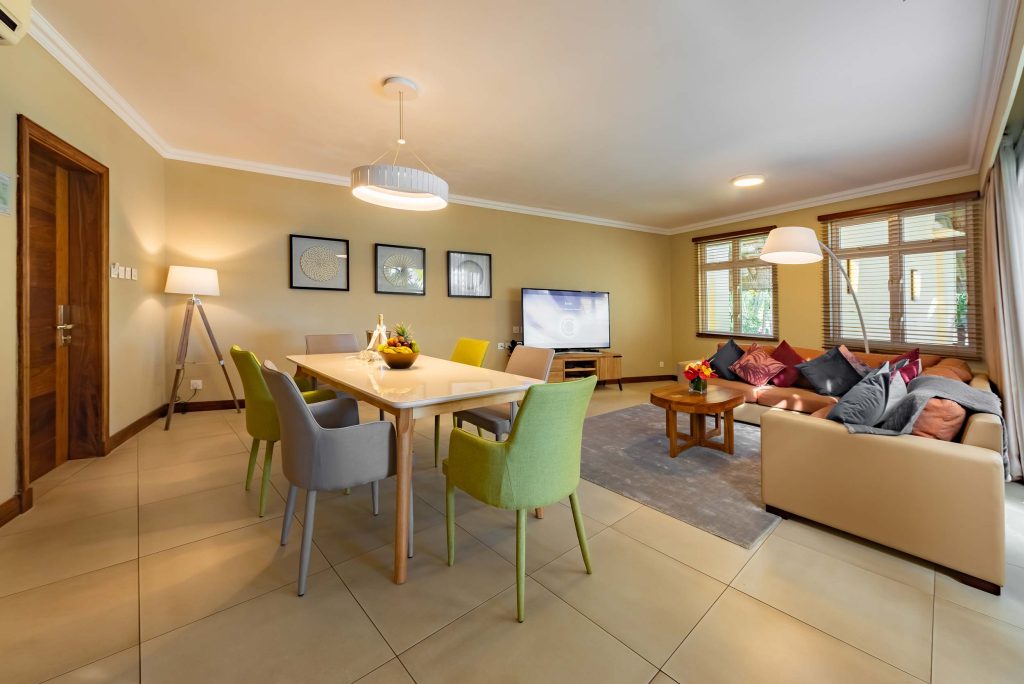 Wohn- und Essbereich mit Holztisch, grauen und grünen Stühlen, cremefarbenem Sofa und großen Fenstern
