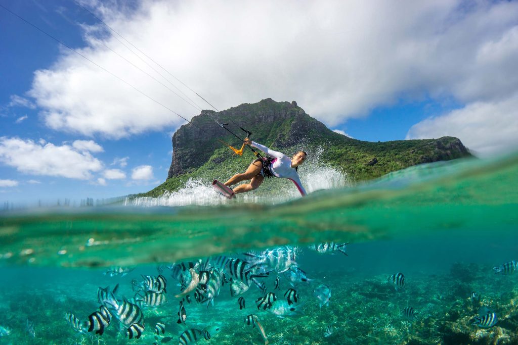 Person kitesurfend auf türkisfarbenem Wasser mit Fischen unter Wasser und grünem Berg im Hintergrund auf Mauritius