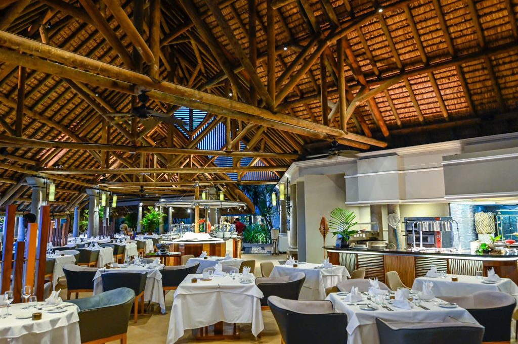 Speisesaal mit weißen Tischdecken, Holzstreben und warmem Licht im Sands Suites Resort & Spa auf Mauritius