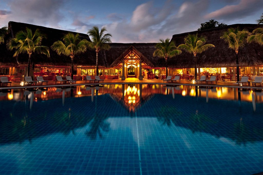 Abendlicher Blick auf Sands Suites Resort & Spa mit großem Pool, Palmen und strohgedeckten Dächern in Mauritius
