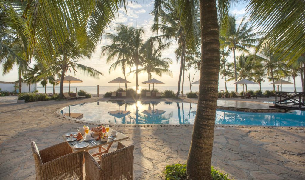 Sultan Sands Island Resort & Spa Außenbereich auf Sansibar Außenbereich mit Swimmingpool, Palmen, geflochtenen Stühlen und gedecktem Frühstück im Sultan Sands Island Resort & Spa