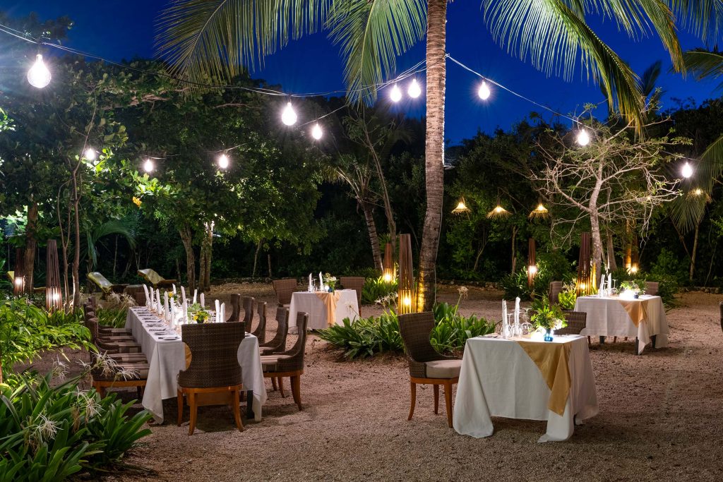 Außenbereich eines Restaurants mit weißen Tischdecken, Kerzen, Rattanstühlen und Glühbirnenbeleuchtung