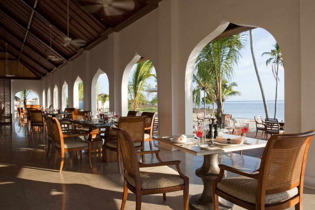 Offener Restaurantbereich mit großen Rundbögen, Holzmöbeln und Blick auf das Meer bei The Residence Zanzibar