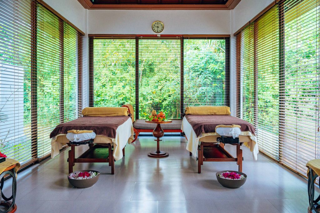 Wellnessraum mit zwei cremefarbenen Massageliegen, Holzjalousien und Blick auf grüne Pflanzen in Sansibar