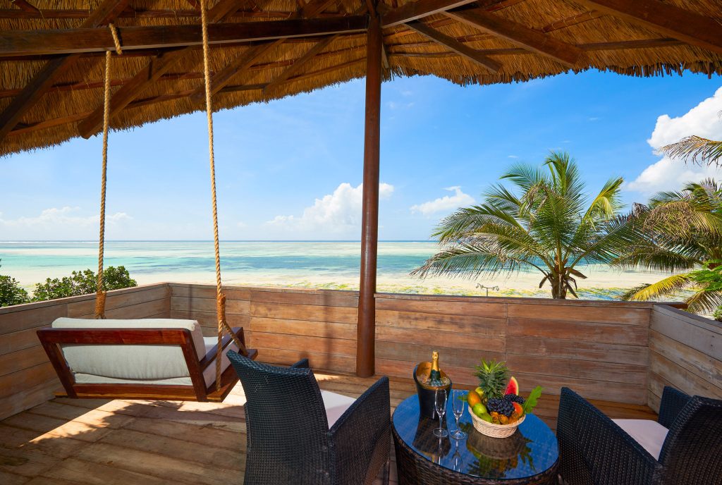 Terrasse mit Holzschaukel, Rattanstühlen und Panoramablick auf tropische Landschaft und Meer bei Tageslicht