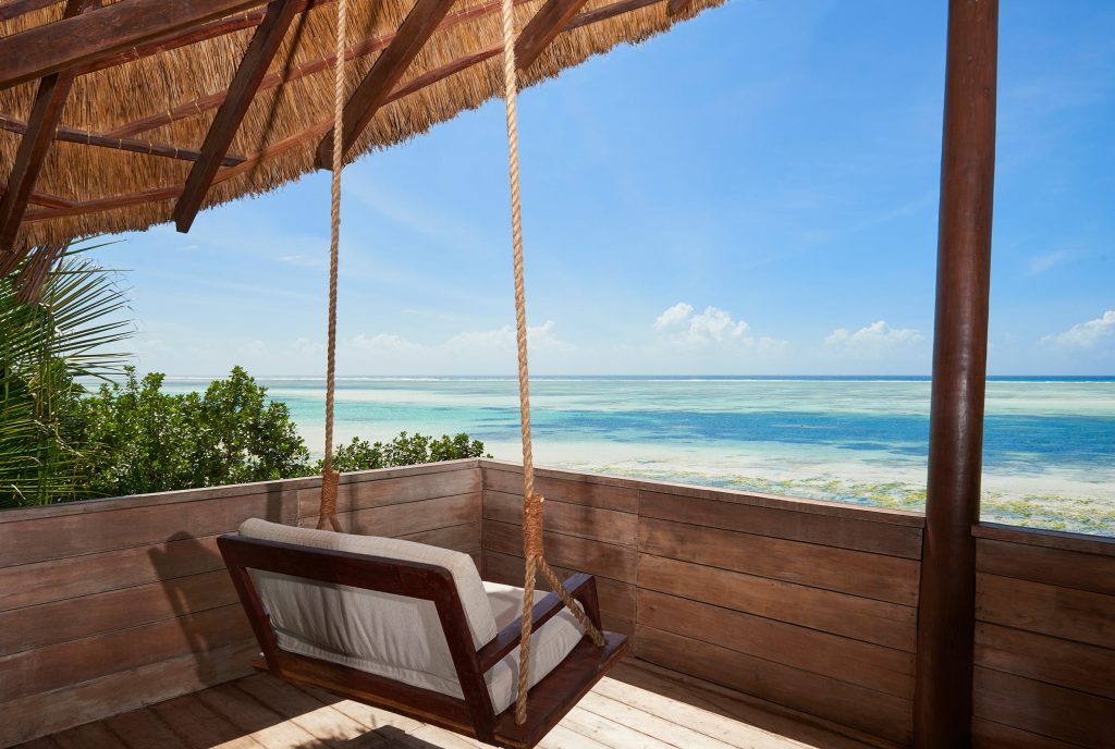 Terrasse mit hölzerner Schaukelbank unter Strohdach und Blick auf das blaue Meer bei Melia Zanzibar