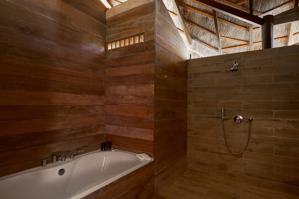Badezimmer mit Badewanne, offener Dusche und Holzdielen an Wänden und Boden im Melia Zanzibar