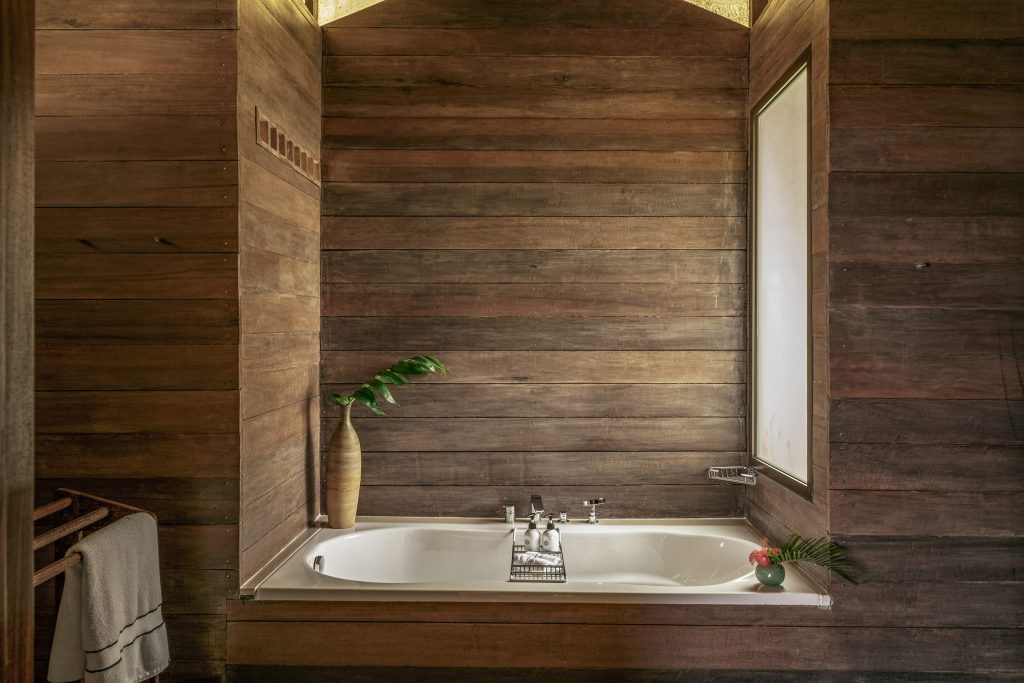 Badezimmer mit eingebauter Badewanne, Holzverkleidung, Vasen mit Blättern und milchglasfenster auf Sansibar