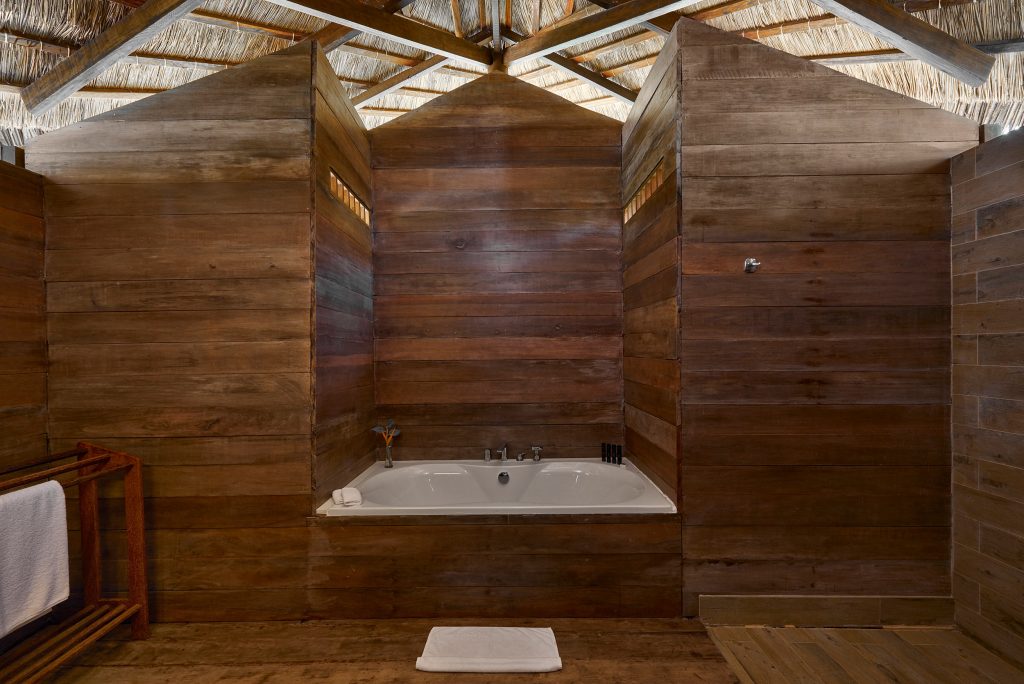 Rustikaler Innenraum mit freistehender Badewanne aus Keramik, Holzpaneelen und Strohdach bei Melia Zanzibar