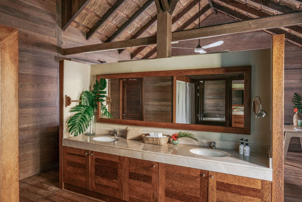 Badezimmer mit groben Holzwänden, Doppelwaschbecken, großem Spiegel und Tageslicht von rechts