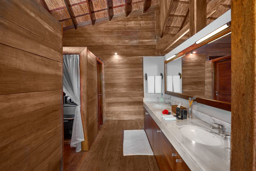 Badezimmer im Melia Zanzibar mit Holzfußboden, weißen Marmortisch, zwei Spiegeln und natürlichen Materialien