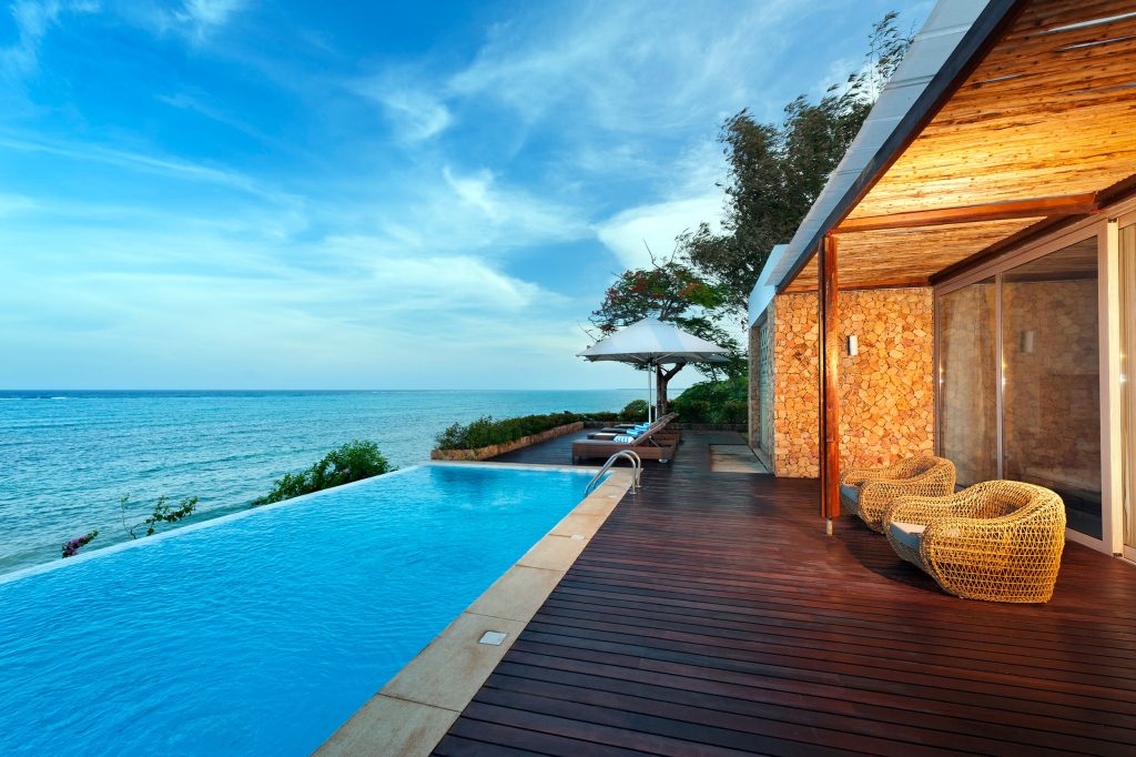 Hotelterrasse mit Holzfußboden und Natursteinwänden, Infinity-Pool und Sicht auf den Ozean