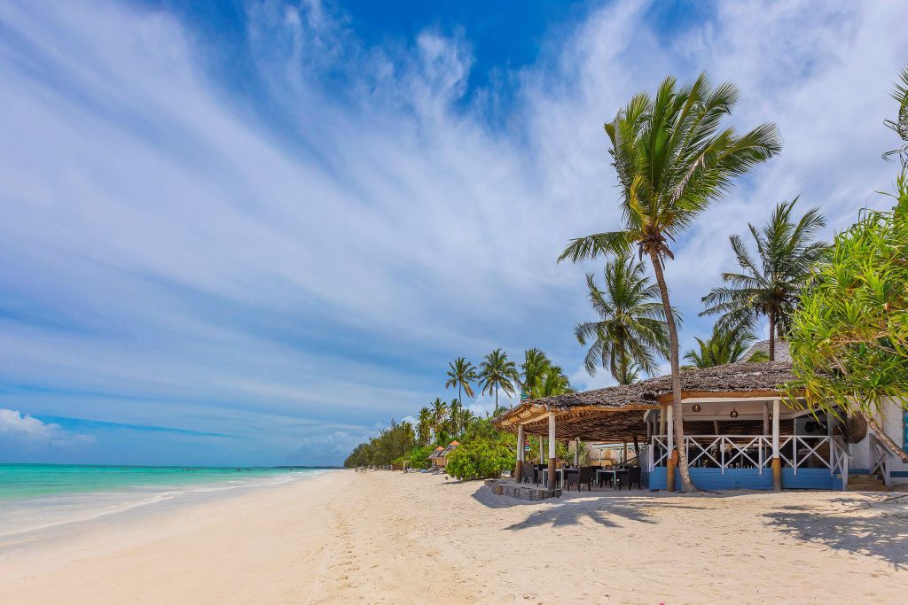 Melia Zanzibar Strand mit Palmen und Strandbar Tropischer Strand mit weißen Sand, türkisblauem Ozean, Palmen und einem strohgedeckten Gebäude am rechten Rand