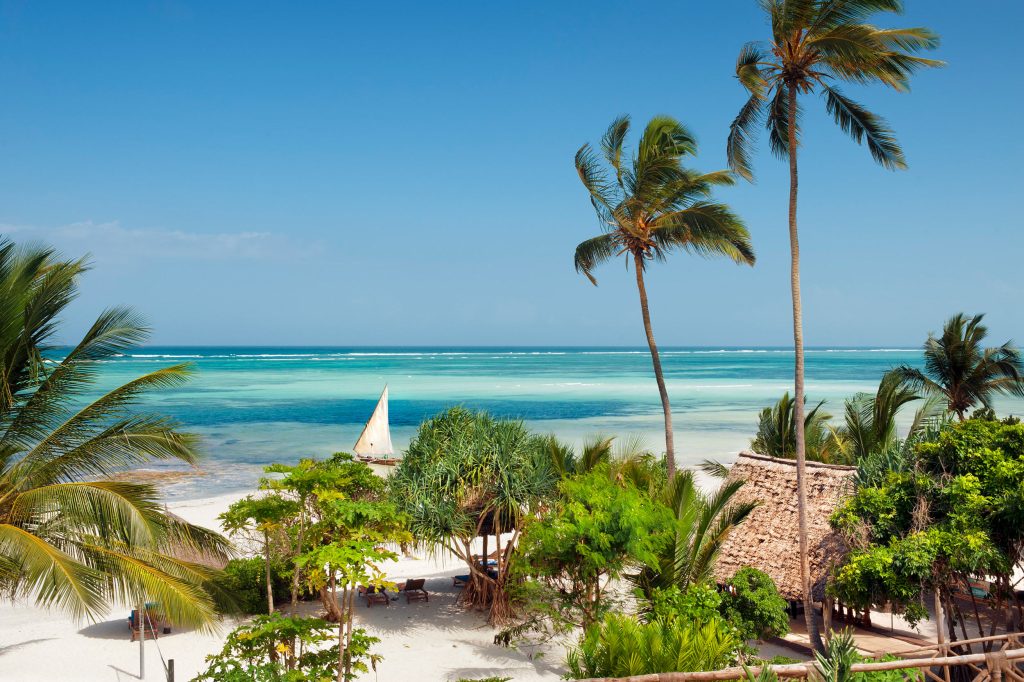 Tropischer Strand mit weißem Sand, grünen Palmen und türkisem Meer bei Melia Zanzibar