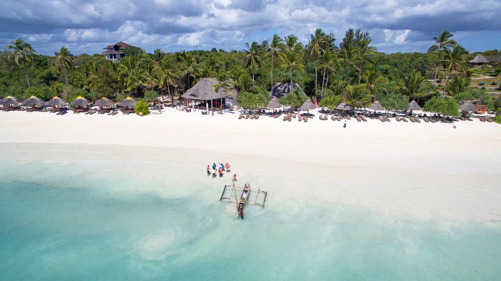 Strand mit weißen Sand und strohgedeckten Sonnenschirmen vor dem Melia Zanzibar Hotel, türkisfarbenes Meer im Vordergrund